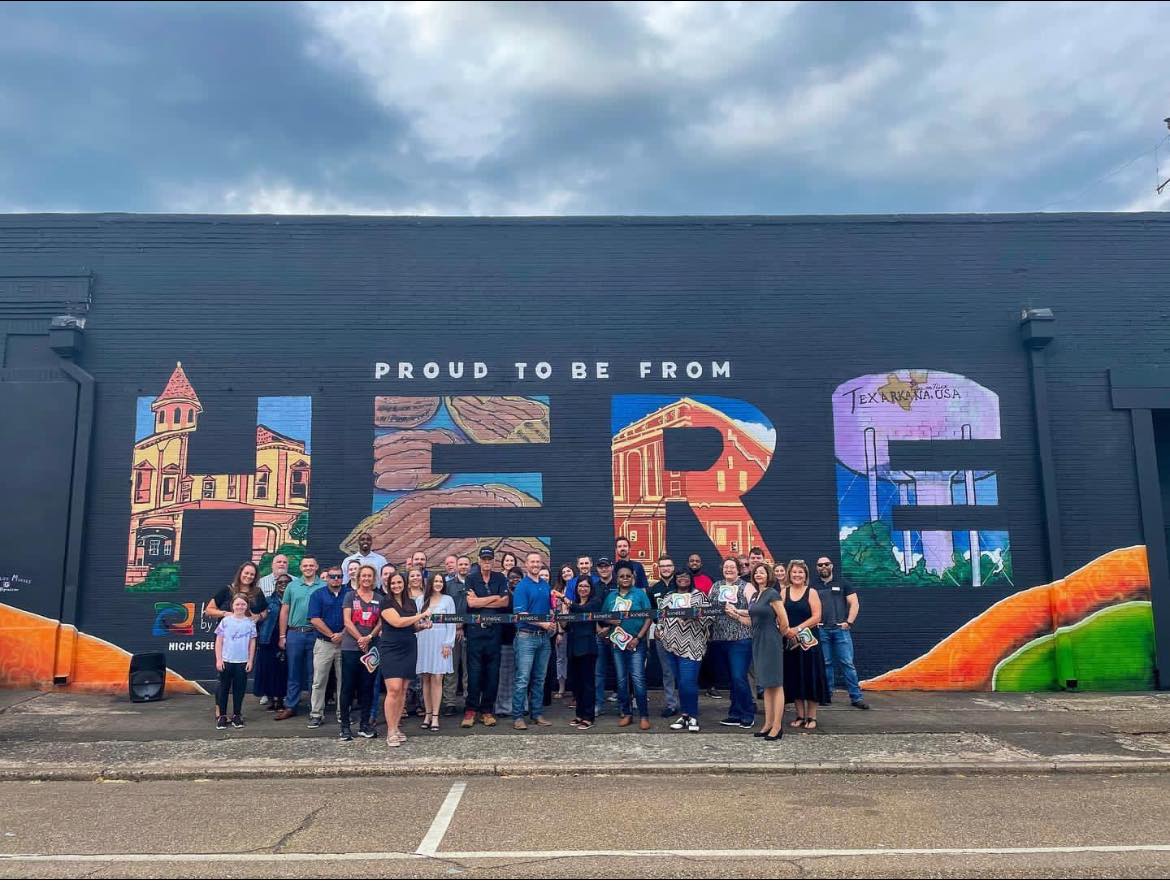 Crowd posing for a photo infront of HERE mural in downtown texarkana, texas